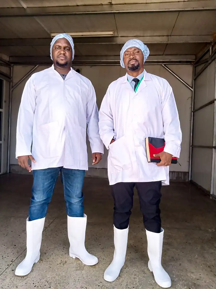 Two people wearing white work coats and boots.