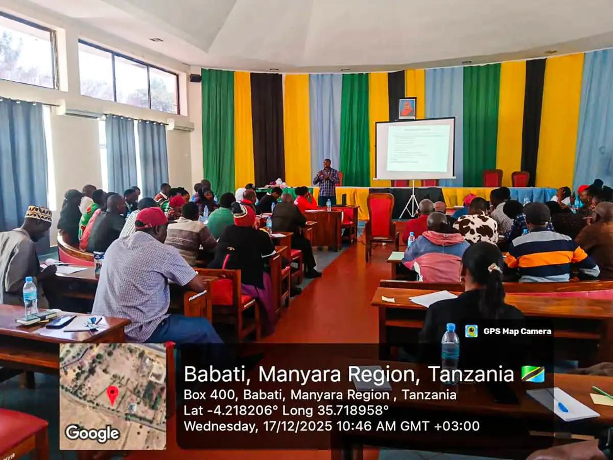 A presenter addresses a seated group; a location and timestamp overlay covers the lower part of the image.